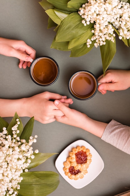 Las manos de los niños sostienen tazas de té y entre sí. Encuentro y té. Vista superior y vertical