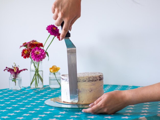 Las manos nivelan la crema con una espátula y cubren el pastel redondo.