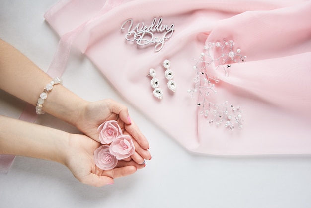 Manos de novia con accesorio de boda y flores decorativas de tela en gasa rosa sobre papel blanco