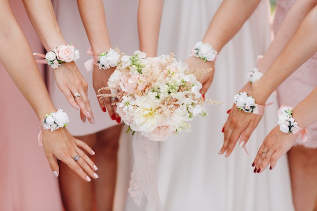 Manos de la novia y damas de honor con flores en tono rosa.