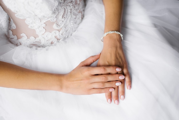 las manos de la novia están en el vestido blanco de boda, manicura de boda