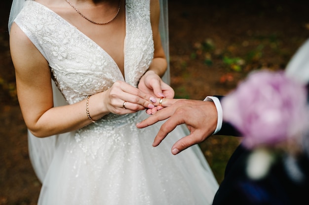Las manos de la novia lleva un anillo de compromiso de boda en el dedo del novio. Ceremonia de boda en la naturaleza. Joyería. de cerca. Recién casados.