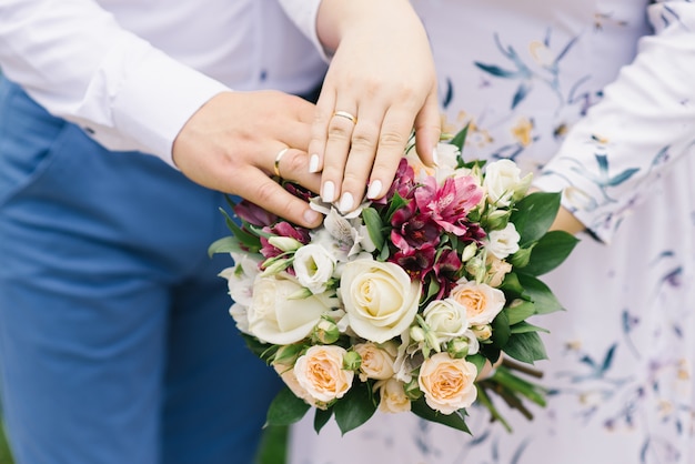 Las manos de la novia y el novio con anillos de boda se encuentran en el ramo de flores brillantes. Matrimonio por muchos años