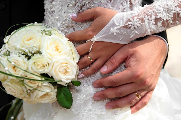 Manos de la novia y el novio con anillos de boda y ramo de rosas