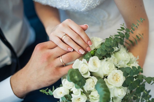 Manos de la novia y el novio con anillos en un ramo de boda