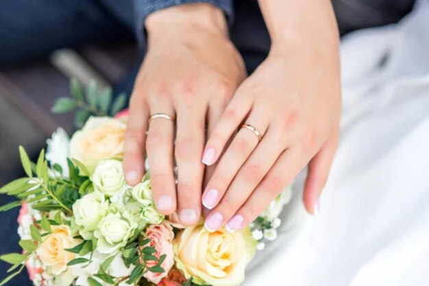 Las manos de la novia y el novio con anillos en el ramo de bodas