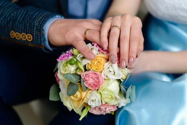 manos de la novia y el novio con anillos se toman de la mano con un ramo