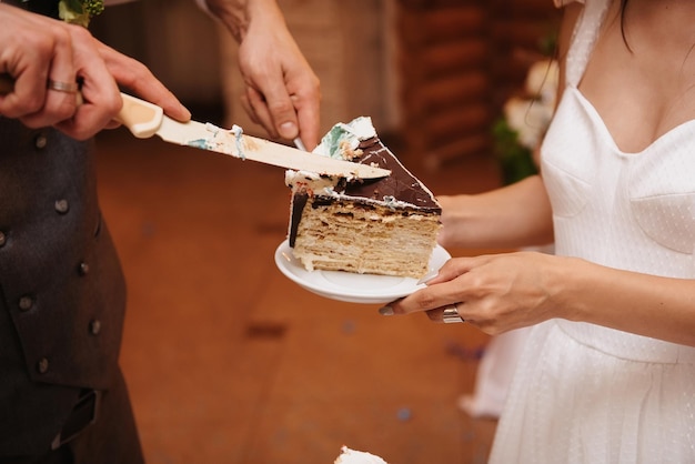 Manos de la novia y el novio con un cuchillo cortan en pedazos un pastel de bodas