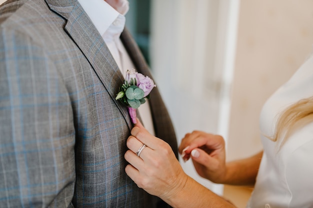 Las manos de la novia ponen al novio en la chaqueta de una boda en el ojal. Concepto de boda.