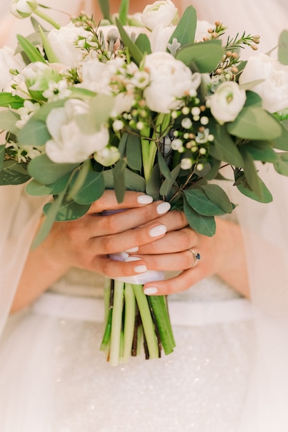 Las manos de la novia sostienen un hermoso ramo de rosas blancas.
