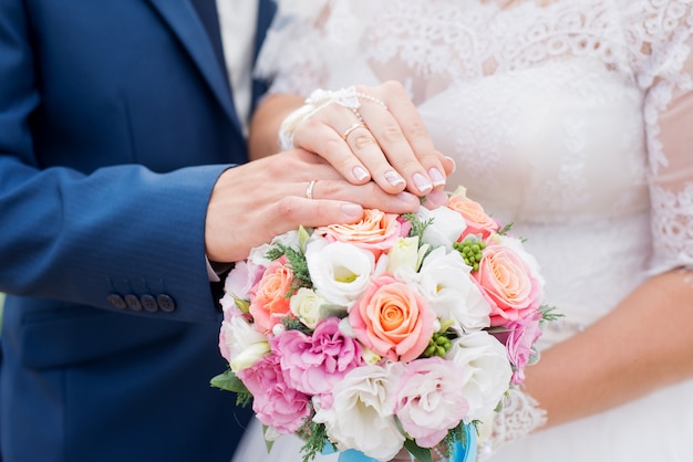 Manos de novio y novia con anillos de boda y ramo de flores.