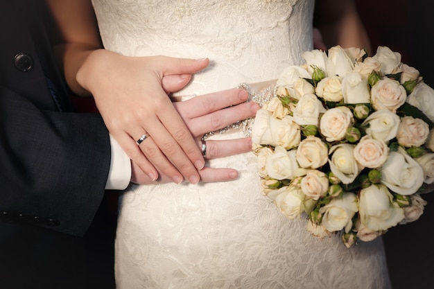 Manos del novio y la novia con anillos de boda y un ramo de rosas