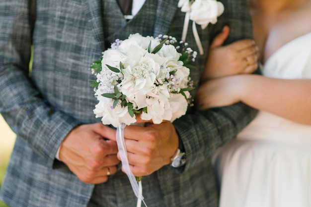 Manos del novio con un ramo de flores de boda