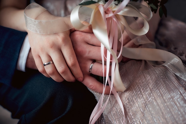 Manos de los novios con anillos de boda y bouquet