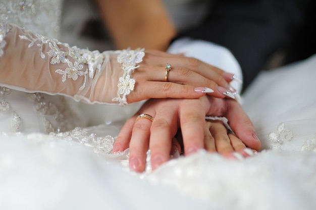 Manos de novios con anillos en el vestido.