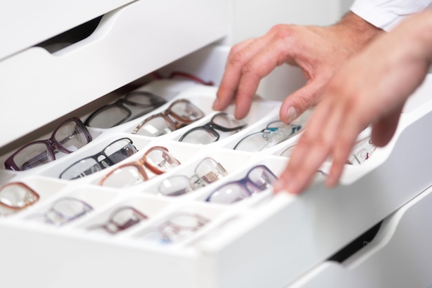 Las manos del oftalmólogo se cierran de cerca, eligiendo gafas de un cajón en la tienda de óptica.