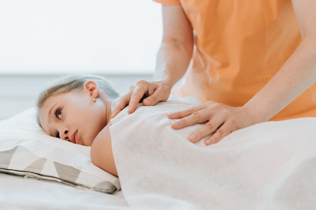 Las manos del osteópata médico real hacen terapia fisiológica y emocional para una niña de ocho años. Sesión de tratamiento de osteopatía pediátrica. medicina alternativa. cuidando la salud del niño