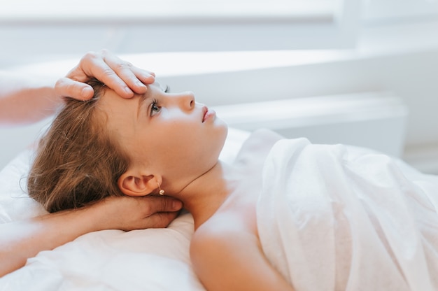 Foto las manos del osteópata médico real hacen terapia fisiológica y emocional para una niña de ocho años. sesión de tratamiento de osteopatía pediátrica. medicina alternativa. cuidando la salud del niño