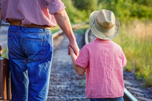 Manos de padre e hijo con sombrero de vaquero cerca del ferrocarril con maleta