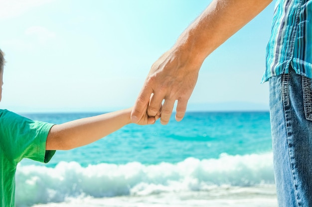 Manos de un padre feliz y un niño a la orilla del mar en un viaje de viaje en la naturaleza