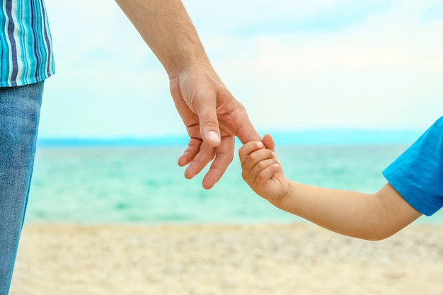 manos de un padre y un hijo junto al mar