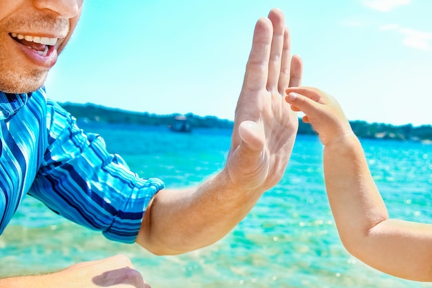 Manos de un padre y un niño felices en la naturaleza junto al mar en un fondo de viaje