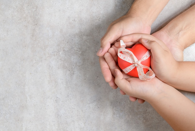 Manos del padre y del niño que llevan a cabo el corazón rojo