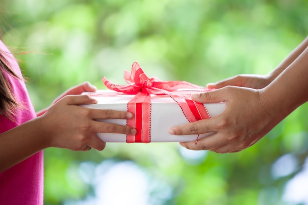 Manos del padre que da el regalo de la Navidad a la muchacha del niño en fondo verde de la naturaleza. Concepto de Navidad.