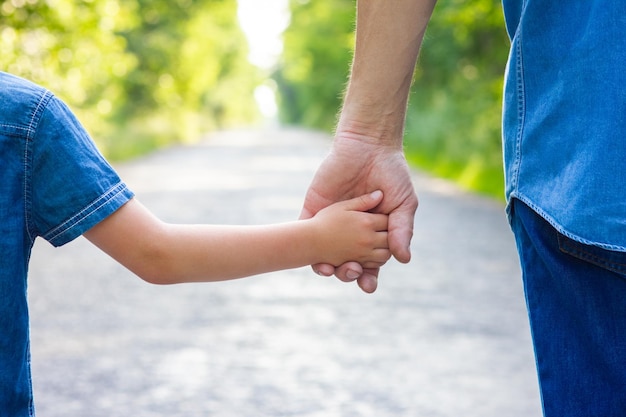 Manos de padres e hijos felices en la naturaleza en la carretera en el fondo del parque