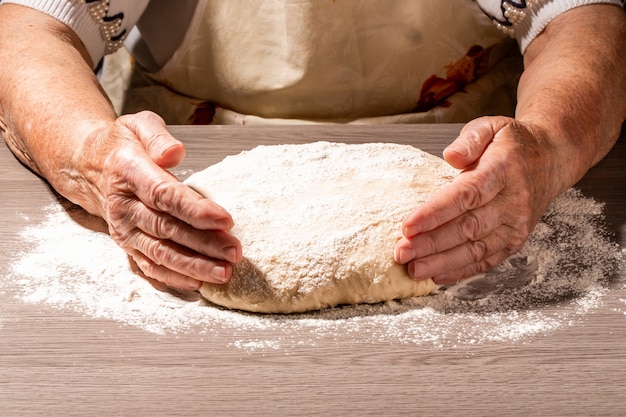 Manos del panadero que hacen la masa en el tablero de madera en cocina. Mujer bisabuela amasa masa para hornear en casa