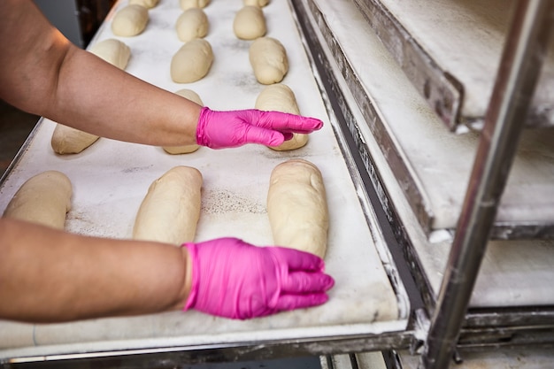 Foto las manos de los panaderos forman la masa para hornear pan y la ponen en la bandeja del horno en la fabricación.