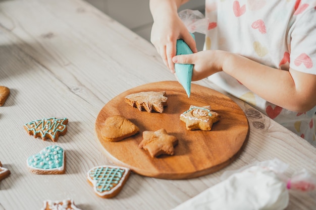 Manos parcialmente borrosas de niña decoran galletas de jengibre con glaseado azul en la cocina. Niño prepara galletas