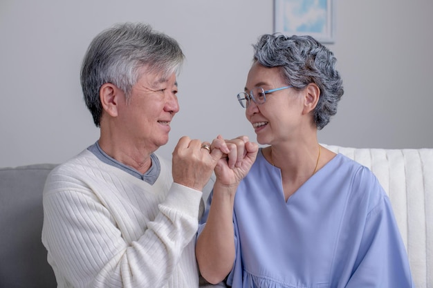 Las manos de una pareja de ancianos asiáticos muestran el dedo meñique en el sofá de la casa Concepto de amor romántico Mano a meñique jurar meñique prometer señales de mano