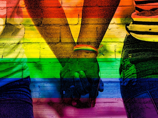 Foto manos de una pareja femenina lesbiana irreconocible con fondo de arco iris lgbt concepto de relación de amor