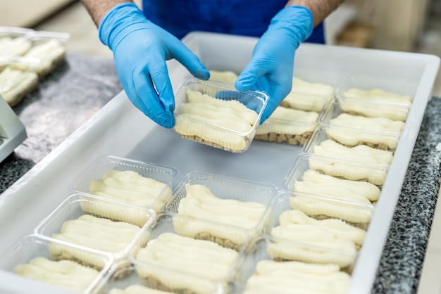 Manos de pasteleros con postres en paquete de plástico poniéndolo para congelar. Fabricación industrial de alimentos