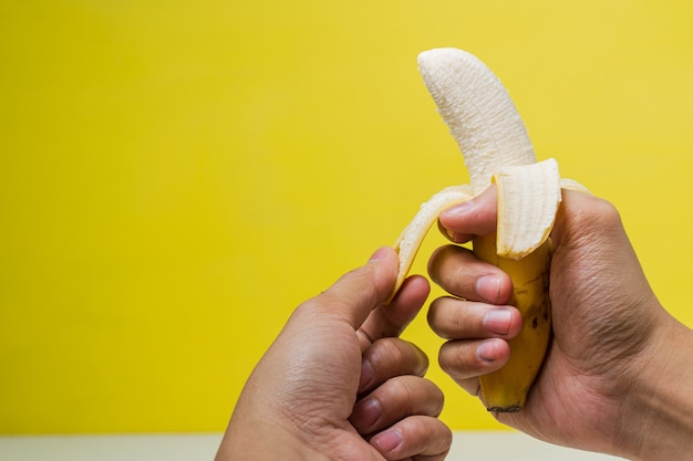 Manos pelando plátano aislado sobre fondo amarillo