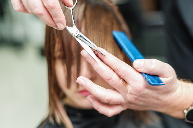 Manos de peluquería cortando el cabello de mujer joven