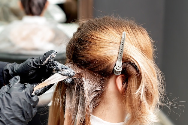 Manos de peluquero en guantes negros teñir el cabello de mujer. Coloración del cabello.