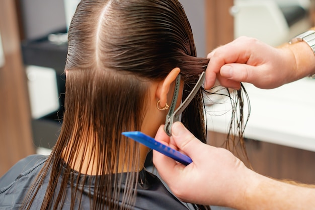 Foto manos de peluquero peina el cabello de mujer joven en peluquería