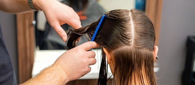 Manos de un peluquero peinando el cabello de una mujer joven dividida en secciones en la barbería