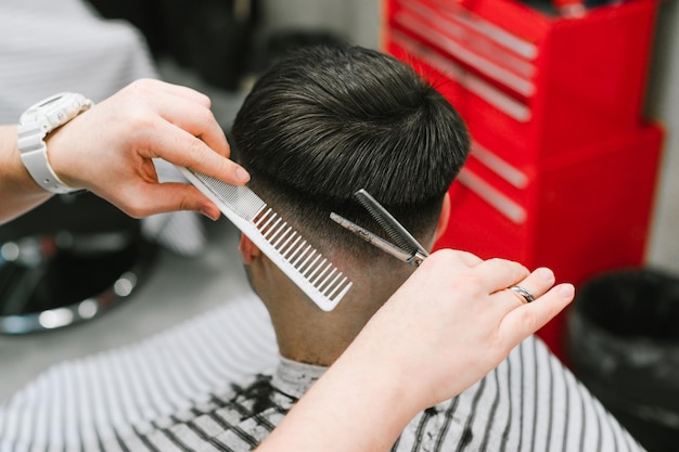 Manos de un peluquero profesional con tijeras y peine peina el cabello de un hombre moreno cerca de la foto