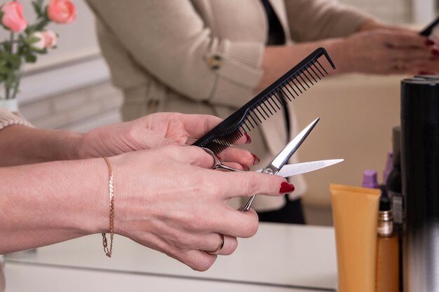 Manos de peluquero sosteniendo tijeras para corte de pelo y cepillo en peluquería