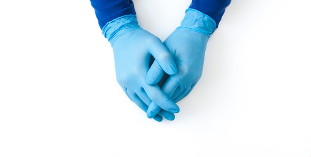 Manos de una persona en los guantes de látex azul sobre mesa blanca