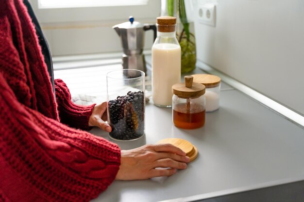 Foto las manos de una persona irreconocible abriendo un frasco lleno de granos de café para preparar el desayuno en una cocina