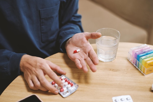 Foto manos de una persona que toma una píldora analgésica con un vaso de agua