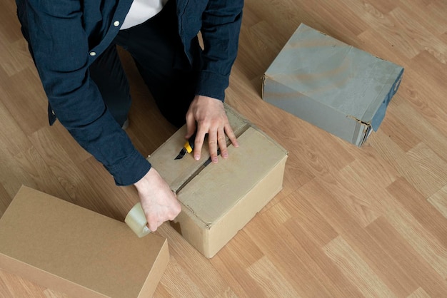 Las manos de la persona sellando una gran caja de cartón con cinta adhesiva para su envíoxA