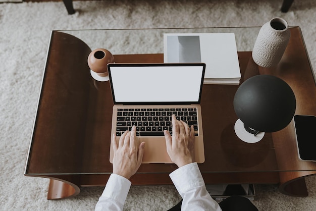 Manos de la persona trabajando en la computadora portátil Espacio de trabajo estético de la oficina en el hogar Trabajo en casa Hoja de papel lámpara de mesa de luz de té Vista plana superior