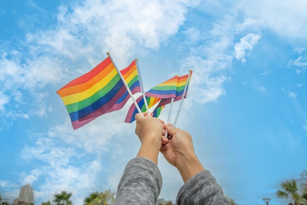 Foto manos de personas de la diversidad levantando banderas coloridas del arco iris lgbtq juntas