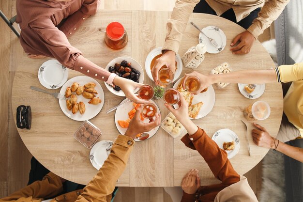Manos de personas sosteniendo un vaso de té y una mesa llena de comida iftar vista superior