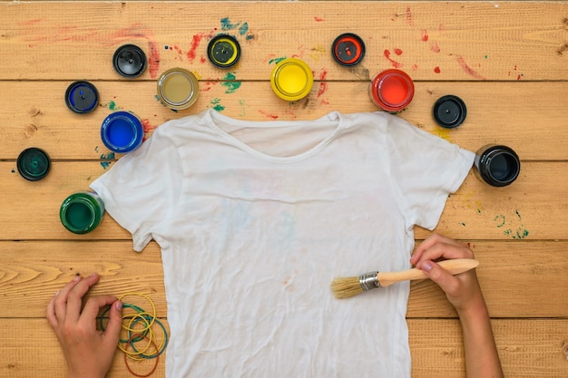 Manos con un pincel y pintura pintan una camiseta blanca